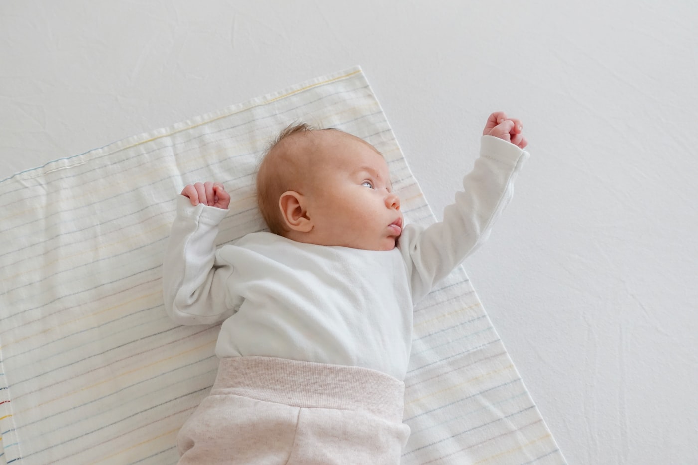 A baby lying awake on their back in a plain bodysuit, on a flat sheet, with nothing else in the sleep space.